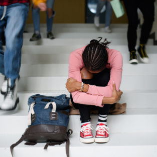A student sits on a staircase with her head on her knees