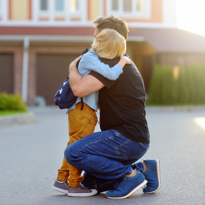 A man comforts a child in front of their house.